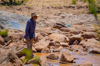 Antananarivo, Madagaskar 07 Ekim 2023 Yaşlı bir adam kızı için küçük bir derede balık yakalar.