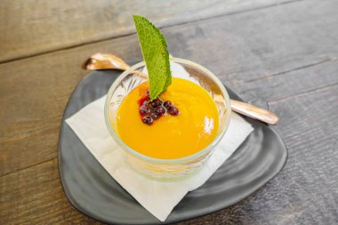 Mango püresi ve düşük geniş bardakta nane yaprağı kaşık ve tabakla servis edilir. Üst görünüm.
