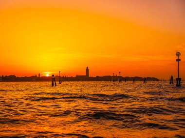 Venedik, İtalya. 29 Ekim 2022 Venedik silueti gün batımında batan güneşin parlak turuncu-kırmızı ışınlarında. Sudan manzara