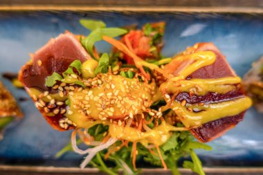 Suşi rulolarının yukarıdan görünüşü. Mavi dikdörtgen seramik tabakta iştah açıcı bir rulo bir restoranda bir masada servis edilir.