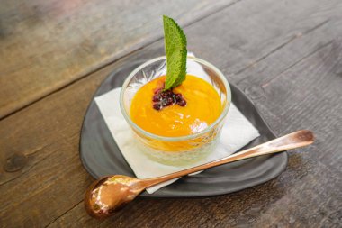 Mango püresi ve düşük geniş bardakta nane yaprağı kaşık ve tabakla servis edilir. Üst görünüm.