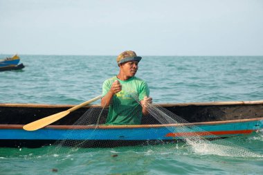 Morondava, Madagaskar. 18 Ekim 2023. Ev yapımı ahşap pirogue teknesindeki kötü niyetli balıkçı ağla balık yakalar. seçici odak, okyanusun yakın görüntüsü