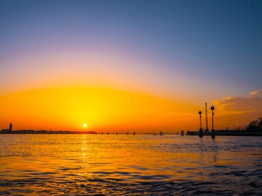 Venedik, İtalya. 29 Ekim 2022 Venedik silueti gün batımında batan güneşin parlak turuncu-kırmızı ışınlarında. Sudan manzara