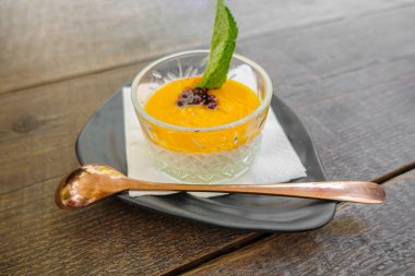 Mango püresi ve düşük geniş bardakta nane yaprağı kaşık ve tabakla servis edilir. Üst görünüm.
