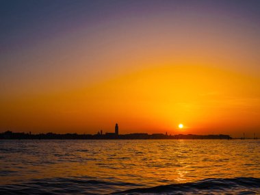 Venedik, İtalya. 29 Ekim 2022 Venedik silueti gün batımında batan güneşin parlak turuncu-kırmızı ışınlarında. Sudan manzara
