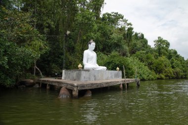 Beruwala,Sri Lanka. 07 Şubat 2023. Beyaz Buda figürü gölün üzerinde oturuyor. Arka plan güzel doğa ağaçları, mavi gökyüzü. Asya seyahati ve din kavramı