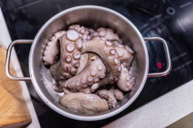 Pişirme işlemi sırasında hafif mutfakta, modern siyah indüksiyon fırınında haşlanmış çiğ ahtapot..