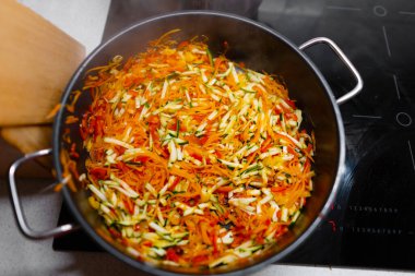 İnce doğranmış renkli mevsimlik sebzelerle büyük yuvarlak, modern bir tava pişirmeye hazır endüksiyon yüzeyinde duruyor.