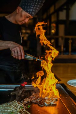 Berlin, Almanya 08. 16 yaşında. 2023. Teppanyaki şefi bir Japon et lokantasında Teppan 'da yemek pişiriyor. Japon şef ateşli bir gösteri sergiliyor ve alev saçıyor