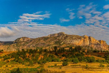 Günbatımında güneşli bir günde Madagaskar yolu boyunca uzanan tepelerin ve dağların güzel manzarası. Küçük evler uzaktan görülebilir. Batan güneşte toprak. Genç bitkilerle dolu pirinç tarlaları