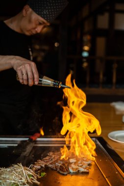 Berlin, Almanya 08. 16 yaşında. 2023. Teppanyaki şefi bir Japon et lokantasında Teppan 'da yemek pişiriyor. Japon şef ateşli bir gösteri sunuyor ve flam yapıyor.