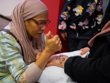 Berlin, Almanya 20.01. 2023 Mehndi ustası kadın eline kına dövmesi çiziyor, mehendi sanat.