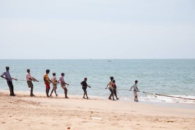 Unawatuna, Sri Lanka 09 february 2023 group of men in summer clothes of different colors helping fishermen to pull over large fishing net from ocean at beach of south Sri Lanka. hard team work. clipart