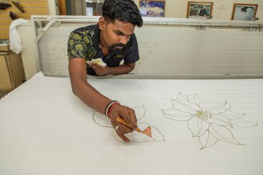 Kuala Lumpur, Malezya. 04.08.2024 genç adam Malasiyan fabrikasında balmumu kalemle geleneksel kalıplar çiziyor. Kuala Lumpur 'daki Batik fabrikası