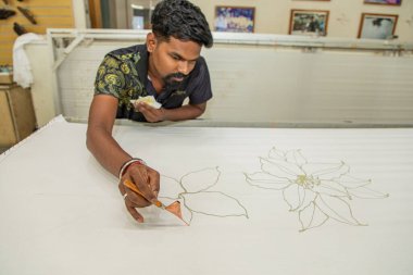 Kuala Lumpur, Malezya. 04.08.2024 genç adam Malasiyan fabrikasında balmumu kalemle geleneksel kalıplar çiziyor. Kuala Lumpur 'daki Batik fabrikası