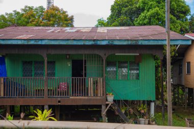 Sandakan, Sabah, Malezya 17.08.2024 geleneksel Malezya evi. Etrafta küçük bir çiftlik ve gölgede evin altında bir araba için yer var.