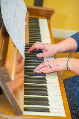 Antika bir piyanonun klavyesinde taşlı altın takılar takan kadın eller. Tanınmayan kadın notalar çalıyor.