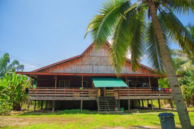 Sandakan, Sabah, Malezya 17.08.2024 geleneksel Malezya evi. Etrafta küçük bir çiftlik ve gölgede evin altında bir araba için yer var.