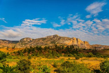 Günbatımında güneşli bir günde Madagaskar yolu boyunca uzanan tepelerin ve dağların güzel manzarası. Küçük evler uzaktan görülebilir. Batan güneşte toprak. Genç bitkilerle dolu pirinç tarlaları