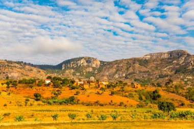 Günbatımında güneşli bir günde Madagaskar yolu boyunca uzanan tepelerin ve dağların güzel manzarası. Küçük evler uzaktan görülebilir. Batan güneşte toprak. Genç bitkilerle dolu pirinç tarlaları