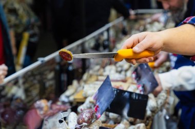 Tanınmayan satıcı bir parça et keser ve tadına bakar. Kurutulmuş sosis pazarı tadıyor..