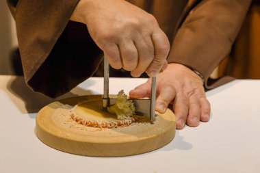 middle section of a middle aged unrecognizable man with hands in monks robe cutting cheese in a certain way clipart