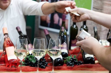 Tanınmayan bir adamın elleri uzanıyor ve şarap standının yanında bir cüzdan tutuyor.