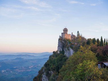 San Marino Cumhuriyeti. Dağdaki 31.10.2022 antik kale. Dar sokaklar turist, restoran ve hediyelik eşya dükkanlarıyla dolu. Aşağıda gün batımında güzel bir dağ manzarası var.