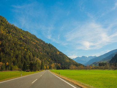 Parlak sonbahar manzarası, Avusturya Alpleri manzarası. Güneşli bir günde İtalya 'ya giden yol. Açık mavi gökyüzü, yamaçlar sonbahar ormanlarıyla kaplı. Dağların arasında terk edilmiş asfalt yol.