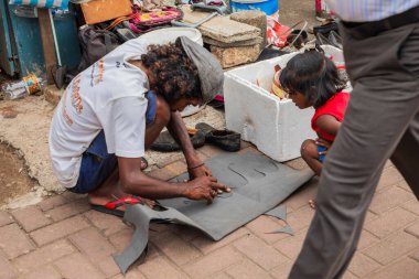Colombo, Sri Lanka 03.02.2023, bir adam koyu renk kumaştan bir şeyler kesiyor ve bir çocuk ne yaptığını izliyor.