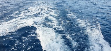 Derin mavi okyanus suyu köpük izleri ve dalgalanmalarla dinamik bir görsel etki yaratır..