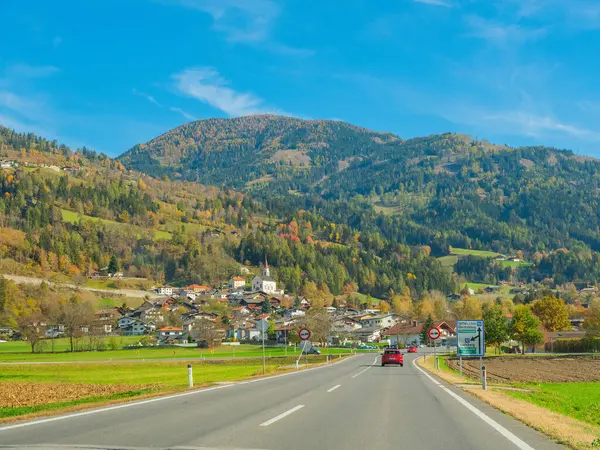 Avusturya, Avrupa. 27.10.2022 sonbahar manzarası, Avusturya Alplerine bakın. İtalya 'ya giden yol açık mavi gökyüzü, yamaçlar sonbahar ormanlarıyla kaplı. Anayolun hemen yanında kilisesi olan küçük bir köy.