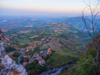 San Marino Cumhuriyeti. Dağdaki 31.10.2022 antik kale. Dar sokaklar turist, restoran ve hediyelik eşya dükkanlarıyla dolu. Aşağıda gün batımında güzel bir dağ manzarası var.