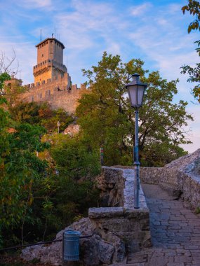 San Marino Cumhuriyeti. Dağdaki 31.10.2022 antik kale. Dar sokaklar turist, restoran ve hediyelik eşya dükkanlarıyla dolu. Aşağıda gün batımında güzel bir dağ manzarası var.
