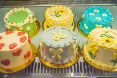 Karmaşık dekorasyonlu çeşitli kekler canlı renkler ve çekici tasarımlarla bir fırın vitrininde sergileniyor..