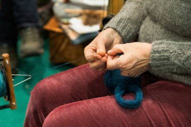 Zanaatkar, renkli iplikler ve aletlerle çevrili, ustaca dönen bir ipliktir, işçiliği ve yaratıcılığı ön plana çıkarır..