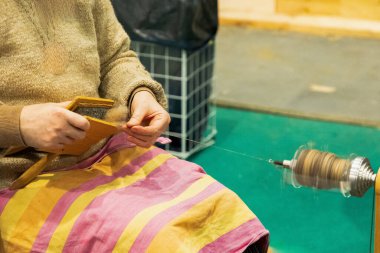 Kadın zanaatkar, geleneksel aletleri kullanarak ustalıkla iplik çeviriyor. Sıcak bir atölye ortamında, sanatçılık ve adanmışlık sergiliyor..