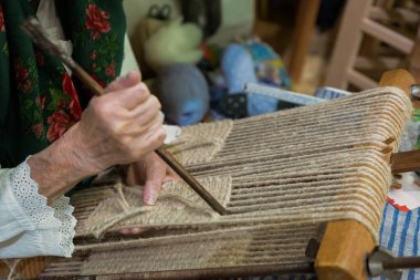 Zanaatkar geleneksel dokuma tezgahında ustaca kumaş dokuyor. Etrafı renkli iplikler ve doğal liflerle çevrili. El işi ve adanmışlık sergiliyor..