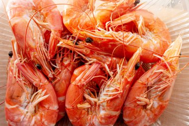 Pişmiş karides şeffaf bir kabın içinde canlı turuncu renklerini ve hassas dokularını vurguluyor. Mutfak sunumları için mükemmel..