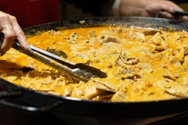 Eller etkin bir şekilde büyük bir tavada lezzetli bir et yemeği karıştırıyor, canlı soslar ve davetkar dokular sergiliyor, sıcak bir atmosfer yaratıyor..