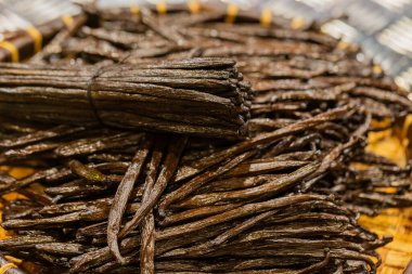 Kurutulmuş vanilya çekirdekleri dokuma sepetinde güzelce düzenlenir, zengin dokularını ve koyu renklerini vurgular, aşçılık kullanımı için mükemmeldir..