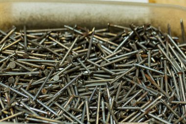 Çeşitli metal çiviler farklı boyutlarda ve şekillerde, endüstriyel donanım ve işçiliğin vurgulandığı bir konteynırda yığılmıştır..