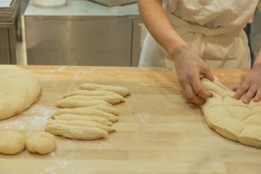 Baker, un ve pişirme aletleriyle çevrili ahşap tezgahta hamuru ustalıkla şekillendiriyor. Lezzetli ekmek yapıyor..
