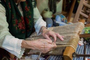 Zanaatkar dokuma tezgahında ustalıkla kumaş dokuyor, canlı iplikler sergiliyor ve rahat bir atölyede ayrıntılı işçilik yapıyor..