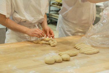 Yetenekli fırıncı ahşap bir yüzeyde hamuru titizlikle şekillendiriyor. Taze malzemeler ve pişirme aletleri ile çevrili. Aşçılık sanatını sergiliyor..