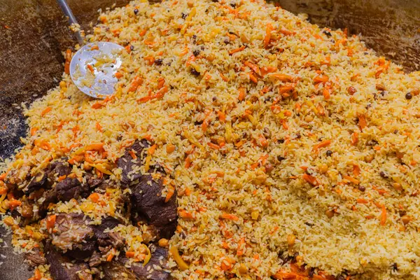 Etli ve sebzeli canlı pirinç tabağı, büyük bir tencerede sunuluyor, mutfak geleneği ve ortak paylaşım.