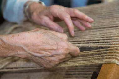 Geleneksel dokuma tezgahında ustalıkla dokuma yapan zanaatkar eller, karmaşık süreci ve işçiliğe olan bağlılığı vurguluyor..