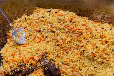 Büyük bir tencerede baharat ve sebzelerin yer aldığı canlı pirinç tabağı, aşçılık hazırlıkları ve zengin dokular sergileniyor..