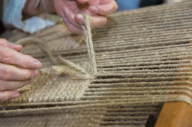 Sanatçının elleri geleneksel dokuma tezgahında ustalıkla doğal iplik dokuyor, karmaşık işçiliği ve kendini adamışlığı vurguluyor..