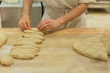 Yetenekli fırıncı, un ve mutfak aletleriyle çevrili ahşap bir tezgahta hamur şekillendiriyor..